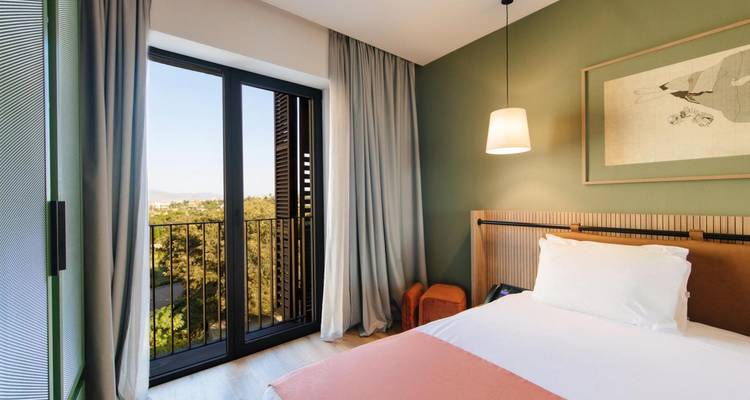 Lichte hotelkamer met groot raam, pastelkleuren en modern minimalistische inrichting.