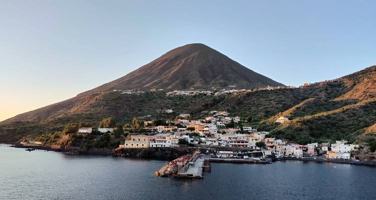 Small coastal village at base of steep volcanic island rising from the sea at dusk