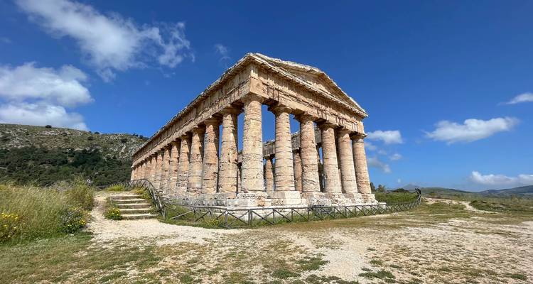 Well-preserved Doric temple set on grassy hillside under bright blue sky in Sicily
