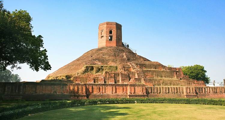 Oude bakstenen stupa die oprijst uit gemanicuurde gazons onder een heldere blauwe hemel.