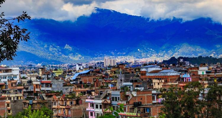 Expansión urbana colorida del Valle de Katmandú enmarcada por montañas verdes exuberantes bajo nubes dramáticas.