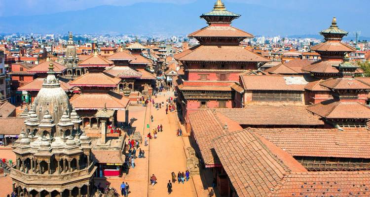 Perspectiva aérea de templos históricos y techos rojos del Valle de Katmandú con montañas azules distantes.
