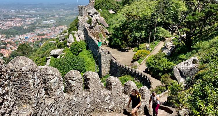 Besucher erklimmen die steinernen Festungsmauern einer mittelalterlichen Gipfelburg mit Panoramablick auf die Stadt unten.
