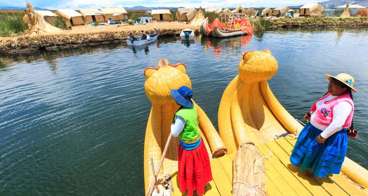 Mujeres indígenas con ropa colorida se encuentran en un muelle de totora junto a barcas de totora con forma de gato en el Lago Titicaca.