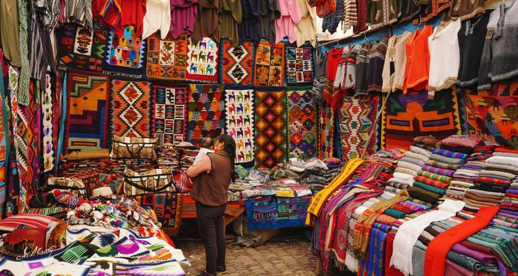Vibrant textile stall packed with colorful woven blankets and garments, one shopper browsing