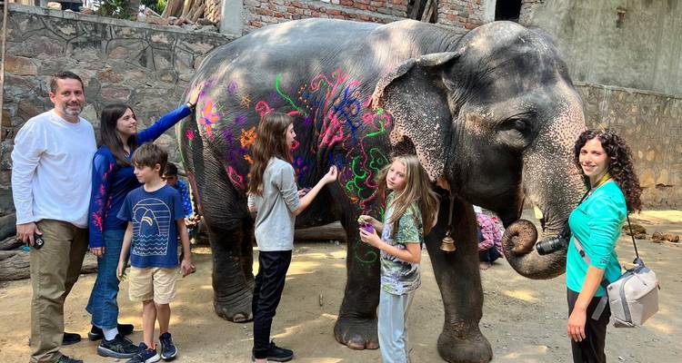Family decorating an elephant with colorful paint patterns in a courtyard