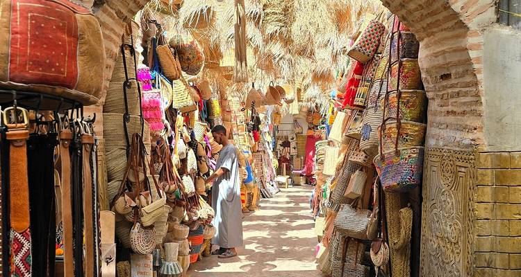 Mercado vibrante en callejón lleno de cestas, textiles y frondas de palmera iluminadas por el sol en el zoco de Marrakech.