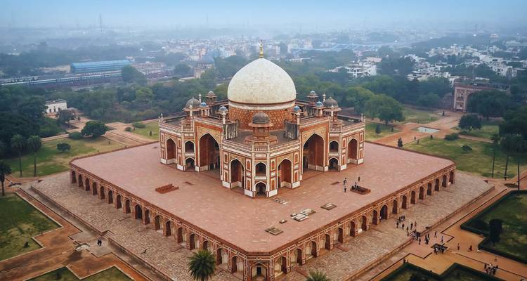 Vista aérea de la Tumba de Humayun rodeada de jardines y bruma urbana.