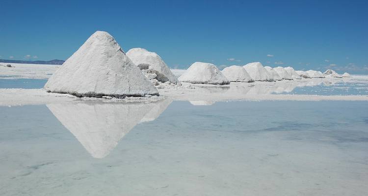 Perfecte witte zoutpiramides en hun reflecties staan op een rij over glinstend water.