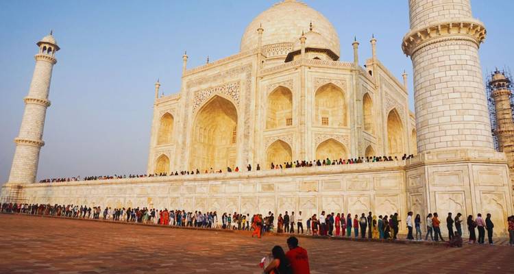 Vista lateral del Taj Mahal con una larga cola de visitantes coloridos alineados en la plataforma de mármol.