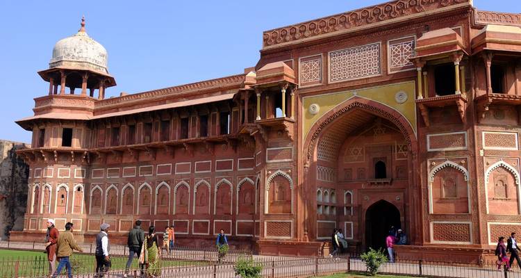 Los visitantes pasean fuera de la grandiosa entrada de arenisca roja y las murallas del Fuerte de Agra bajo un cielo despejado.