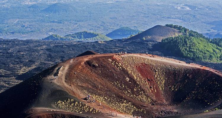 Un cratère volcanique spectaculaire avec des randonneurs debout sur le rebord au milieu de champs de lave noire et rouge sur le mont Etna.