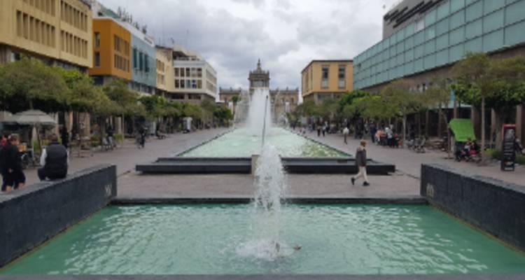 Lange fonteivijver geflankeerd door stadsgebouwen leidt naar een monumentale structuur onder bewolkte hemel.