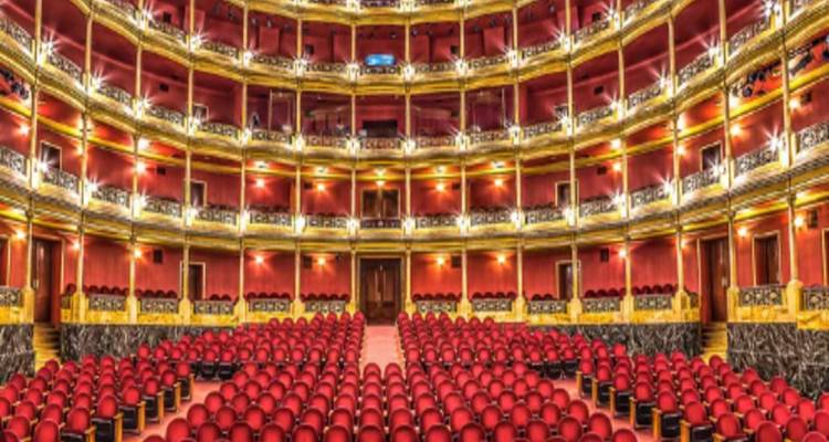 Weelderig theaterinterieur met rijen gouden balkons en rijen rode stoelen.