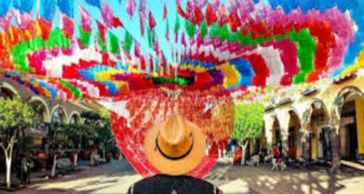 Persoon met sombrero loopt onder een baldakijn van levendige veelkleurige papieren vlaggetjes in een straatmarkt.