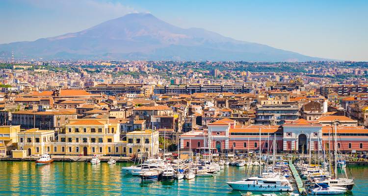 El vibrante puerto de Catania con yates respaldado por el Monte Etna elevándose sobre la ciudad.