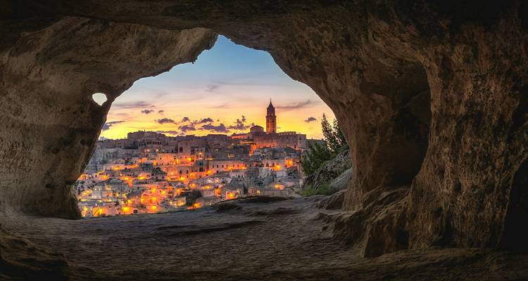 Schemerzicht op Matera's grotwoningen en verlichte skyline omlijst door een natuurlijke grotopening.