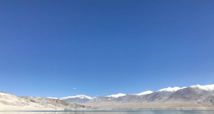 A wide view of desert mountains meeting a tranquil lake under an expansive blue sky.