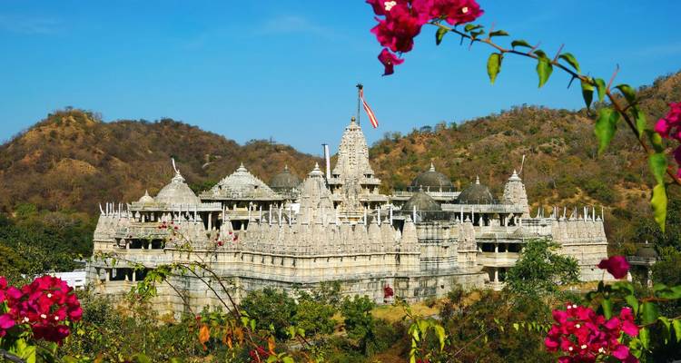 Panoramaaußenansicht des weißen Marmor-Ranakpur-Jain-Tempels, eingebettet in trockene Hügel, umrahmt von rosa Bougainvillea.