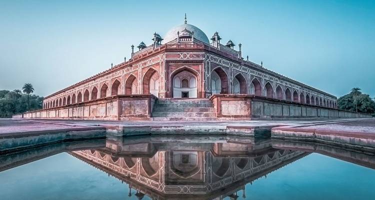 Reflejo simétrico del amanecer de la Tumba de Humayun en un estanque de agua quieta con cielos rosa-azul.