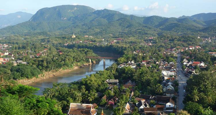Aerial panorama of Luang Prabang’s rooftops, river and lush mountains stretching into the hazy distance.