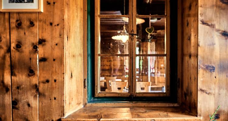 Detalle de un marco de ventana de madera rústica que da a un acogedor interior alpino.