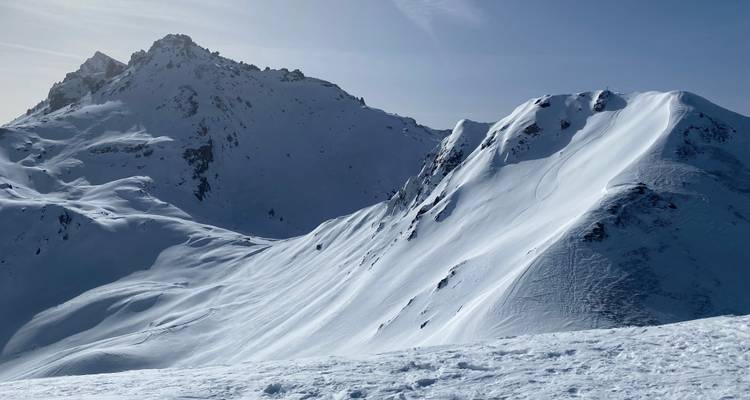 Sharp snowy ridgelines and craggy summits dominate a bright winter alpine scene.