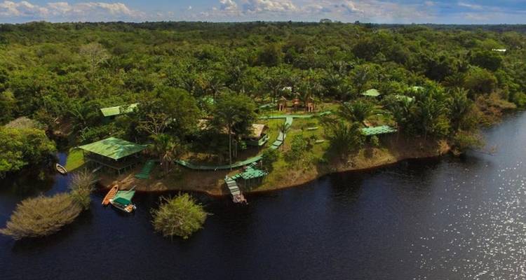 Aerial view of a jungle lodge complex on a lush river island.