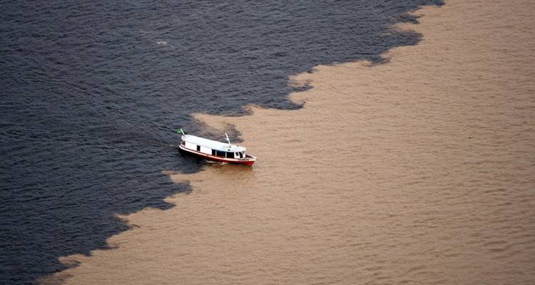 Small boat floats where dark and light Amazon waters meet in striking contrast.