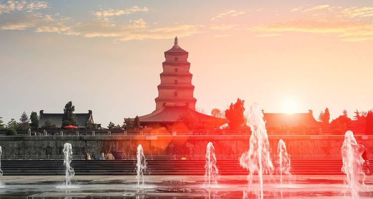 Fountains dancing before the silhouetted Big Wild Goose Pagoda at sunset with warm orange glow