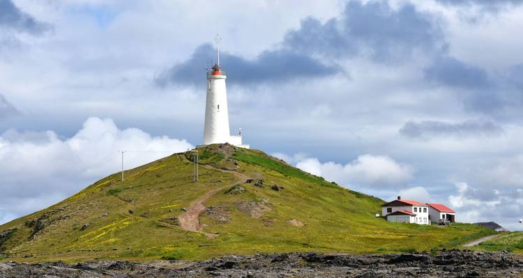Der Leuchtturm Reykjanesviti steht auf einem grasbewachsenen Hügel unter einem teilweise bewölkten Himmel.
