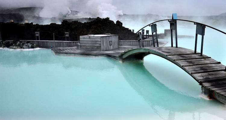 Milky-blue geothermal waters of the Blue Lagoon with wooden footbridge and steaming volcanic rocks.