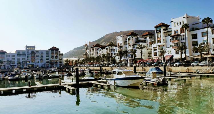 Marina moderna en Agadir con barcos, cafés frente al mar y edificios de apartamentos encalados respaldados por colinas áridas.