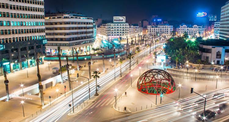 Langzeitbelichtung einer nächtlichen Aufnahme eines Boulevards in der Innenstadt von Casablanca mit Lichtsteifen, Palmen und modern beleuchteten Gebäuden unter einem dunklen Himmel.