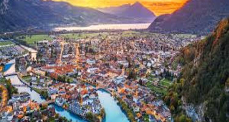 Panoramic aerial view of a Swiss town nestled between lakes and mountains at sunset.