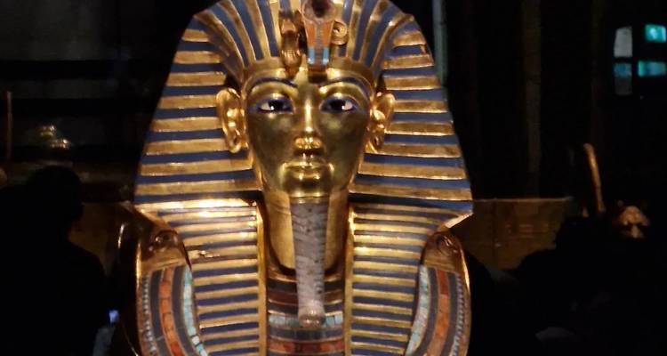 Goldene Totenmaske des Tutanchamun glänzt unter Scheinwerfer in dunkler Galerie