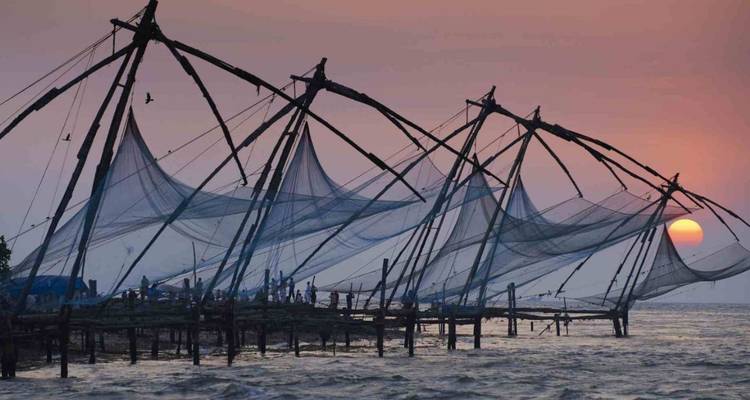 Silhouettierte chinesische Fischernetze erstrecken sich bei Sonnenuntergang über das Arabische Meer, während die orange Sonne zum Horizont hinabsinkt.
