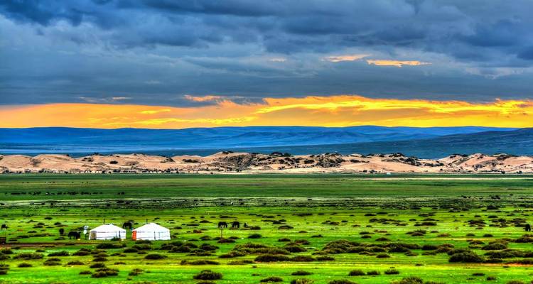 Deux yourtes blanches reposent sur une vaste steppe émeraude avec des dunes lointaines sous un ciel de coucher de soleil dramatique.