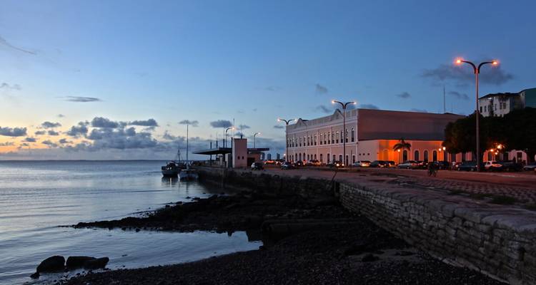 Promenade côtière et bâtiment colonial au crépuscule avec des eaux calmes