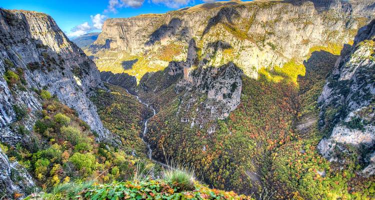 Vue panoramique sur une gorge profonde bordée de falaises calcaires imposantes recouvertes des couleurs d'automne.