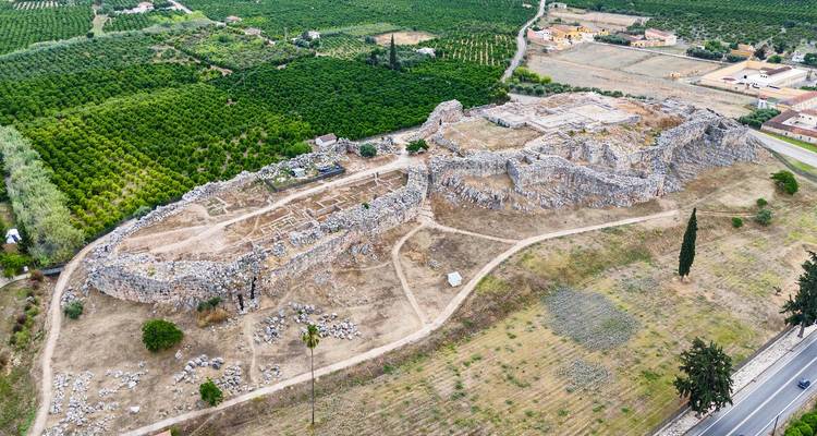Vue de drone de vastes ruines de fortifications en pierre serpentant à travers un paysage rural de vergers and fermes.