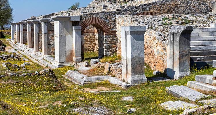 Colonnade en ruines et arcs de pierre d'une cité antique baignés de fleurs sauvages printanières.