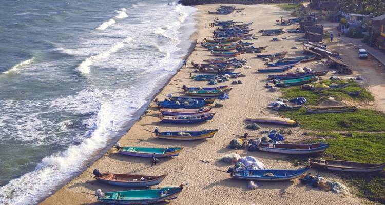 Luftaufnahme von Fischerbooten, die an einem sandigen Ufer neben rollender Brandung an Land gezogen sind.