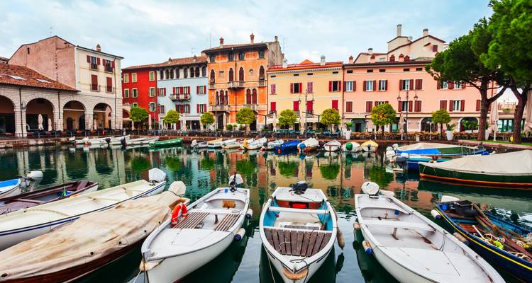 Façades historiques colorées reflétées dans le port tranquille rempli de petits bateaux à Desenzano del Garda.