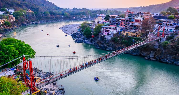 Die überfüllte Hängebrücke Lakshman Jhula überspannt den türkisfarbenen Ganges, während Sonnenuntergangsfarben Rishikesh beleuchten.