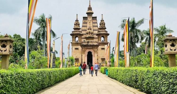 Besucher, die auf einem angelegten Weg zu einem kleinen, verzierten Tempel gehen