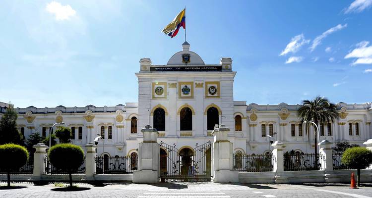 Wit neoklassiek Ministerie van Defensie gebouw in Quito met Ecuador's vlag die trots wappert boven smeedijzeren hekken.