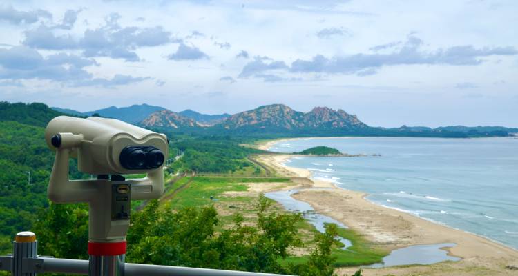 Un télescope d'observation surplombant un littoral accidenté, des collines boisées et des pics de granit lointains sous un ciel partiellement nuageux.