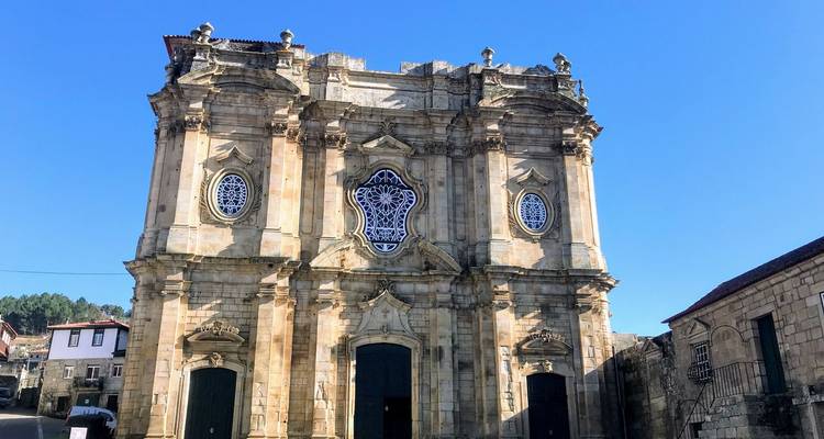 Eine ornamentreiche barocke Kirchenfassade mit hohen Säulen und kunstvollen Steinarbeiten steht unter einem klaren Himmel