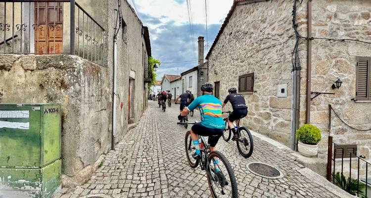 Eine Gruppe von Mountainbikern fährt eine schmale Kopfsteinpflasterstraße entlang, die von Steinhäusern gesäumt ist